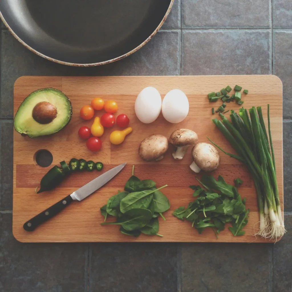 Fresh healthy ingredients including avocado, eggs, mushrooms, tomatoes and green onions on a wooden board